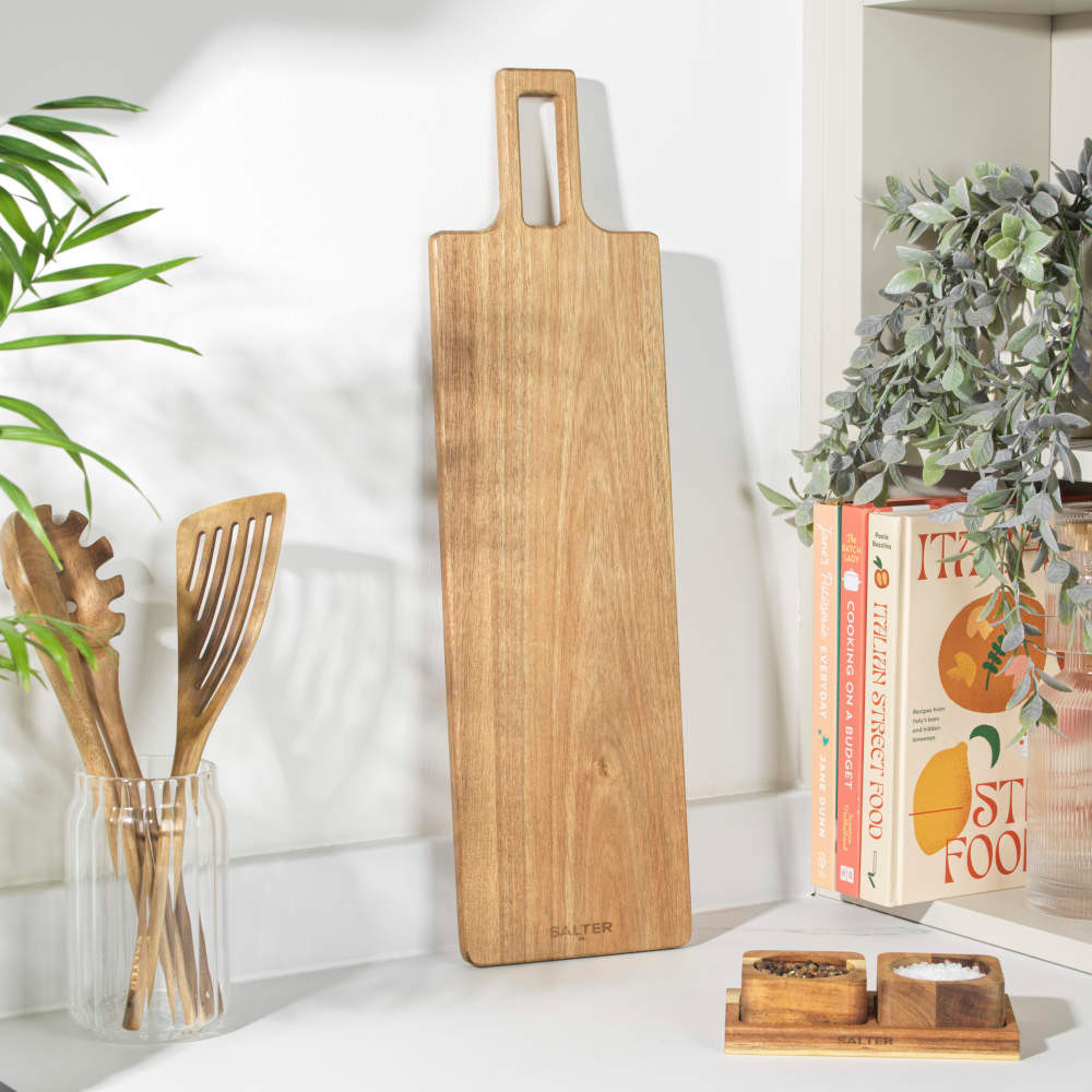 Long rectangular wooden serving board with handle, shown on a kitchen worktop.