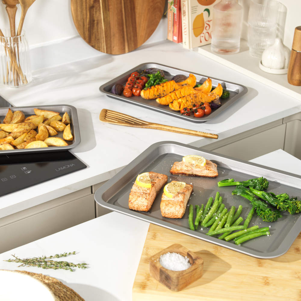 Non-stick oven trays with baked salmon, green veg, potato wedges and roasted tomatoes