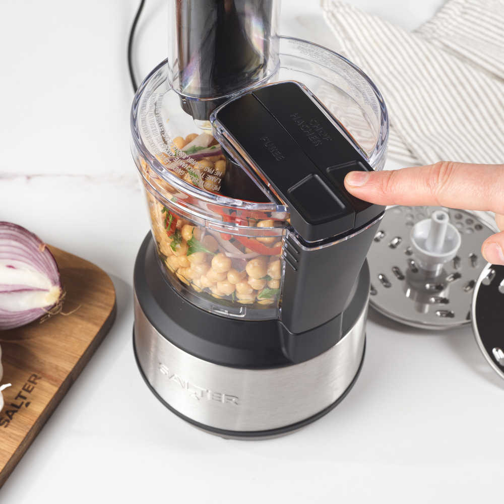 Food processor blending chickpeas and veg, finger pressing button, close-up view