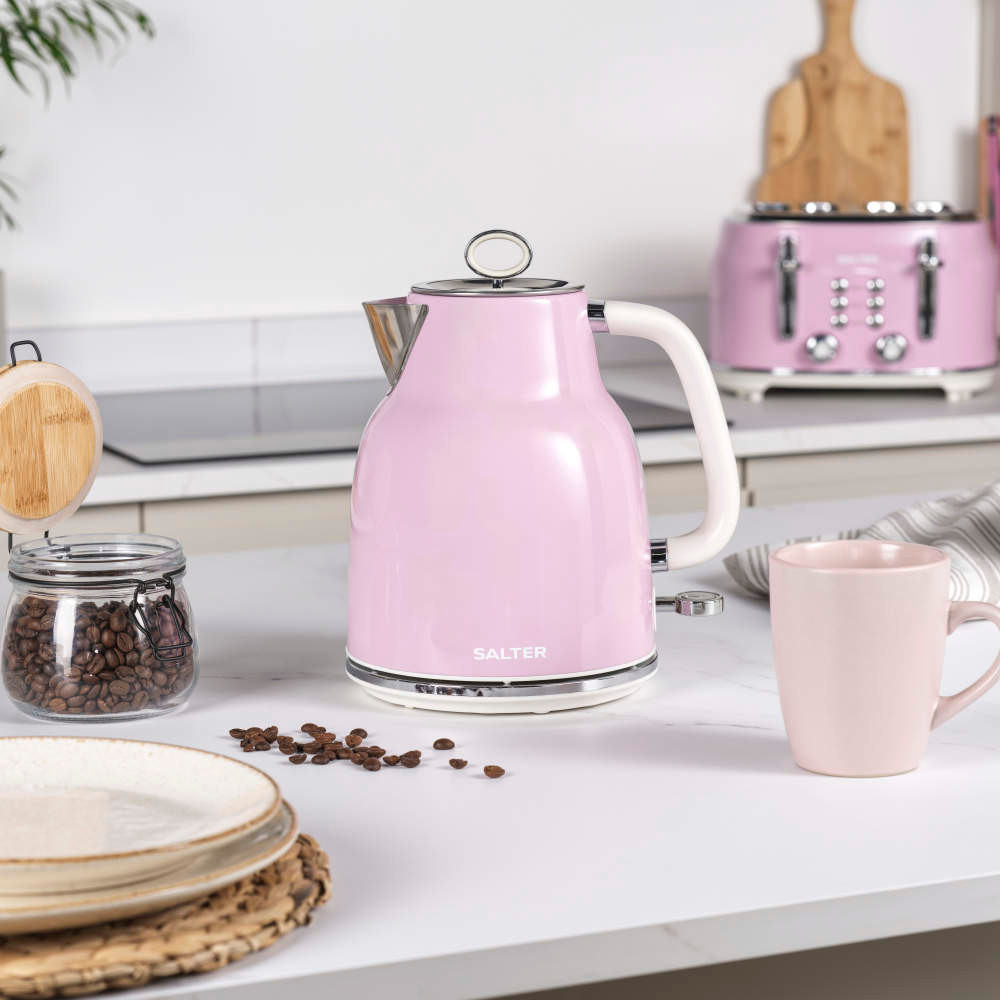 Pink electric kettle with handle on kitchen counter, cup and coffee jar nearby