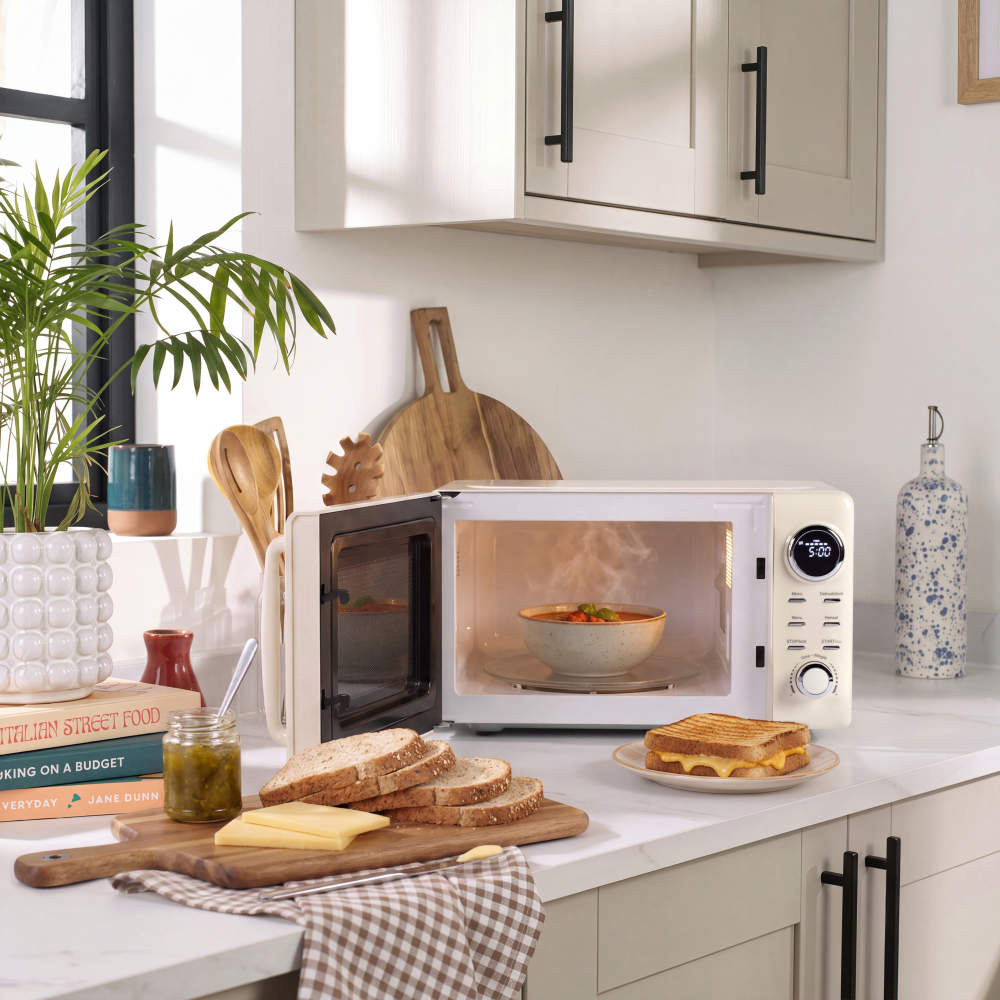 Cream microwave oven on kitchen counter with open door, bowl of soup inside