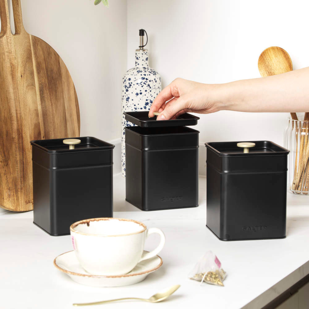 Set of three matte black kitchen storage tins, one with lid open on worktop