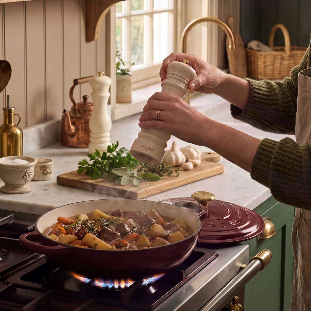 Cream pepper grinder seasoning stew in burgundy cast iron casserole on gas hob