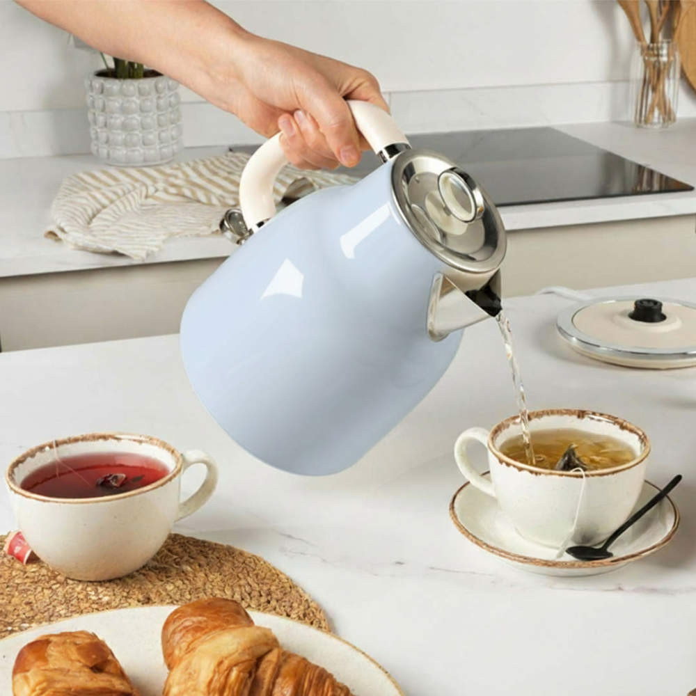 Light blue kettle pouring hot water into teacup on kitchen counter, with croissants and tea.