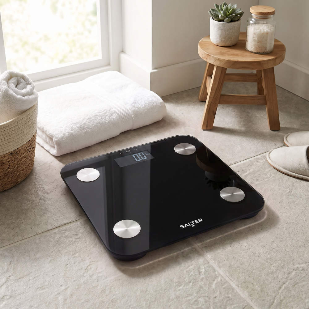 Black digital bathroom scale with silver sensors on tiled floor