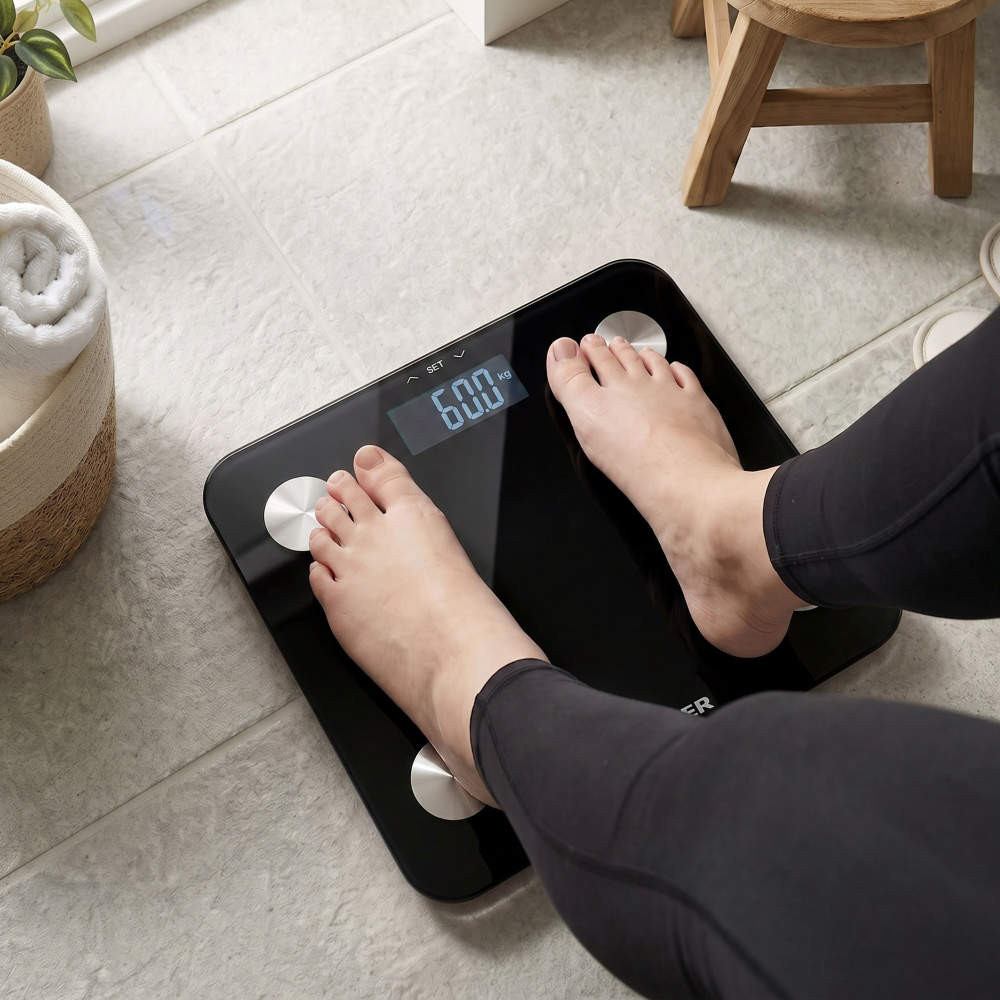 Black digital bathroom scale with feet standing on it, display shows 60.0 kg