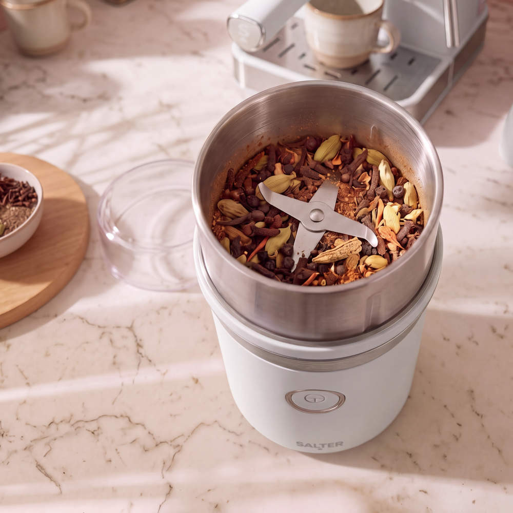 White electric spice grinder with whole spices in stainless steel bowl