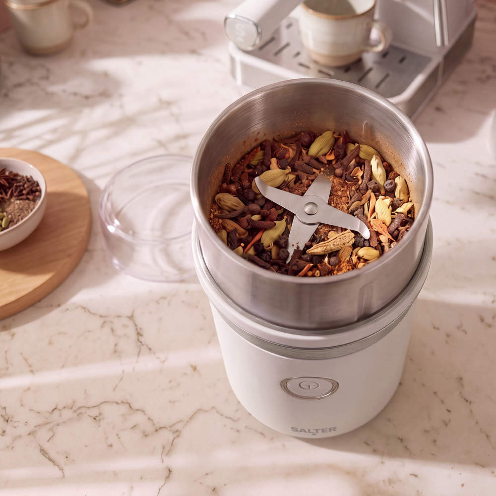 White electric spice grinder with whole spices in stainless steel bowl