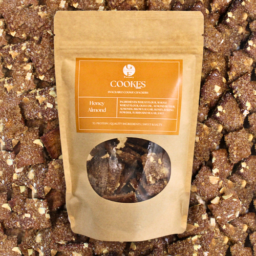 Cookes - Honey Almond by The Granola Factory. The orange and tan bag is on a background of the product, a square Honey Almond looking cracker-cookie.