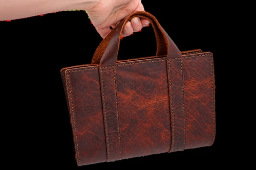 Custom leather Bible cover with carry handle showing the bible cover being held by a hand for size reference.
