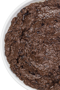 Close-up of rich, chunky black olive tapenade in a white ceramic dish, showing its coarse texture and deep colour. Close-up of rich, chunky black olive tapenade in a white ceramic dish, showing its coarse texture and deep colour.