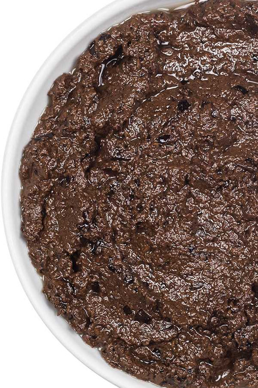 Close-up of rich, chunky black olive tapenade in a white ceramic dish, showing its coarse texture and deep colour.