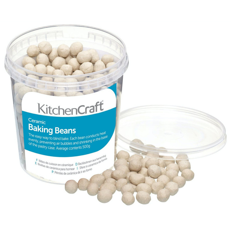 Clear plastic tub of KitchenCraft Ceramic Baking Beans 500g with lid off and beige ceramic baking beans spilling out onto a white surface.