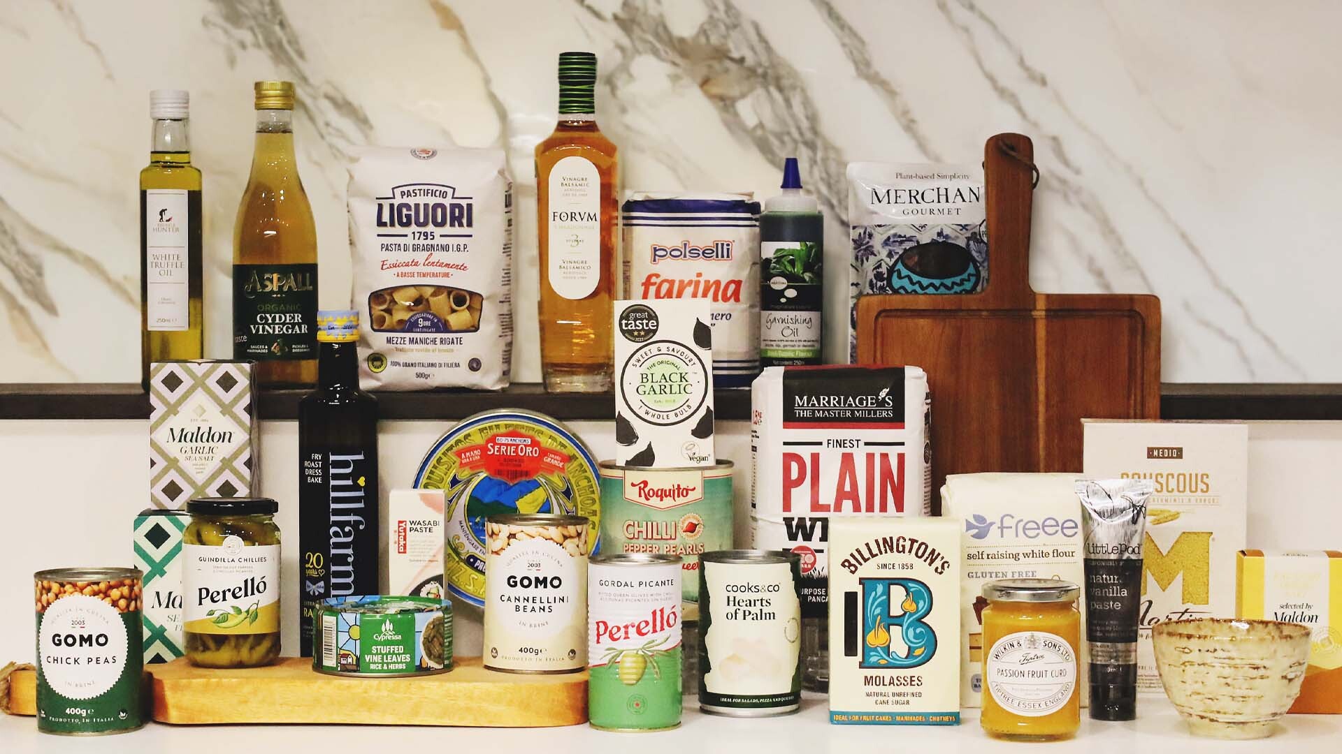 A variety of premium store cupboard ingredients from i4C Infusions4Chefs displayed on a kitchen counter, including oils, flours, pulses, spices, and condiments.