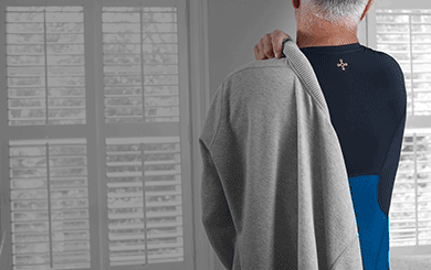 A man wearing a black Lower Back Support Shirt putting on a sweater.