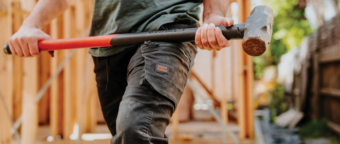 Tradie in Hard Yakka work pants carrying a sledgehammer on a timber frame site