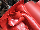 Macro close-up of vermilion oil paint ribboning between mill rollers, highlighting smooth fine-grained texture