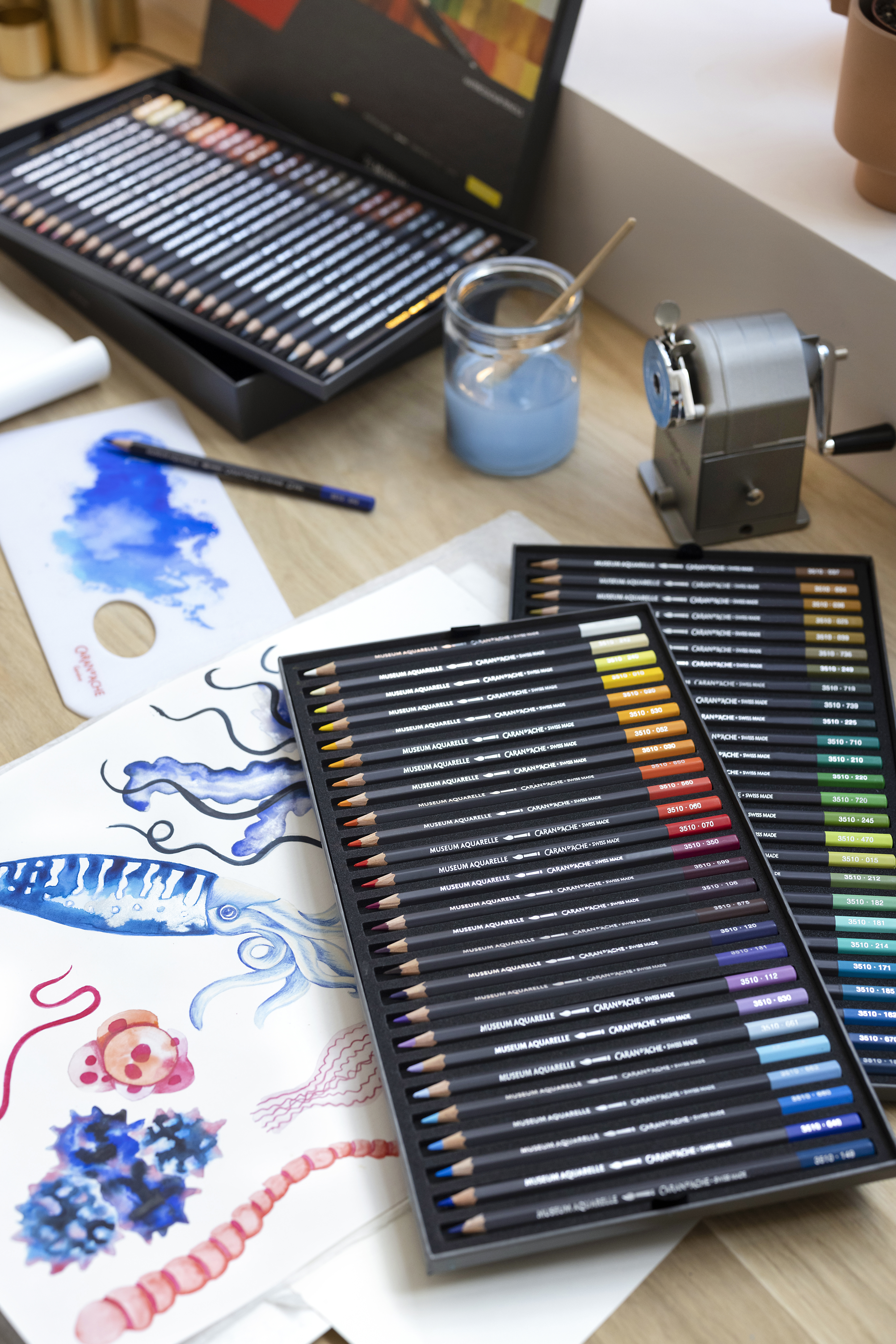 tudio scene with Museum Aquarelle sets, sketches and water jar—Swiss-made water-soluble colour pencils for pros.