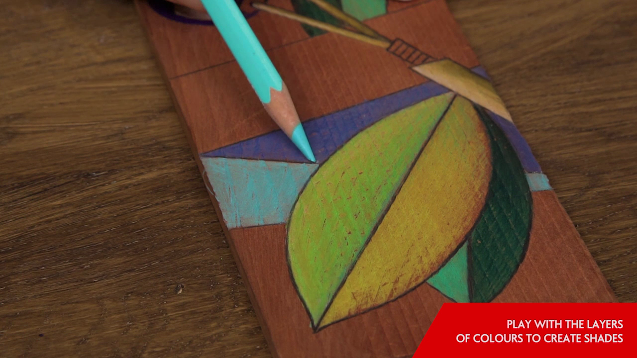Caran d’Ache Pablo coloured pencil adding bright turquoise shading to a leaf illustration on a wooden panel