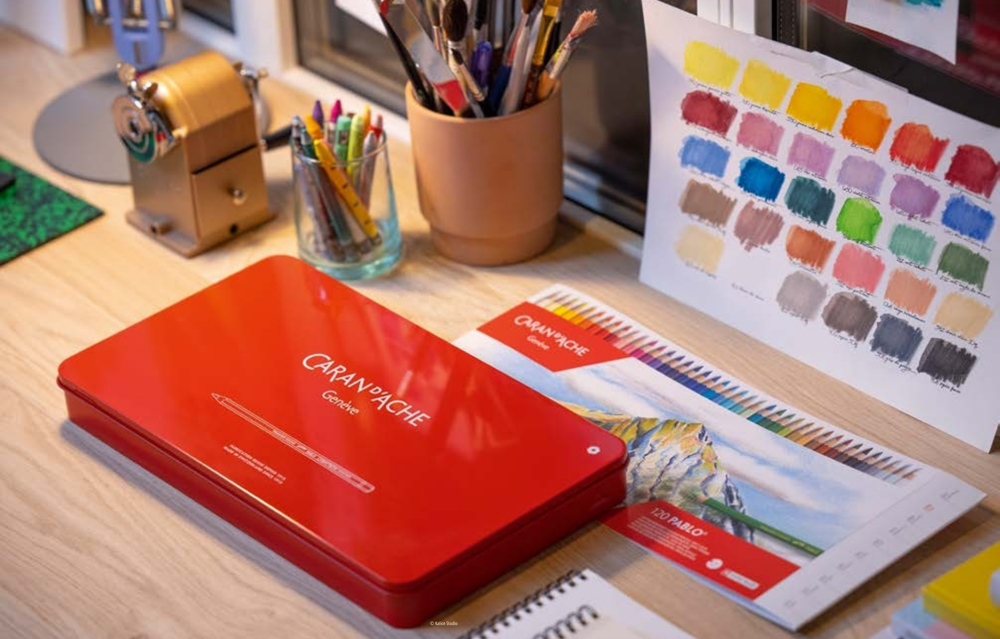 Closed Caran d’Ache Pablo coloured pencil tin on studio desk beside colour chart and art supplies