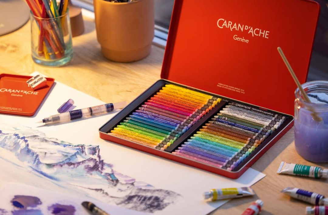 Open Neocolor II Aquarelle tin set on studio desk—rainbow pastels ready for watercolor sketching.