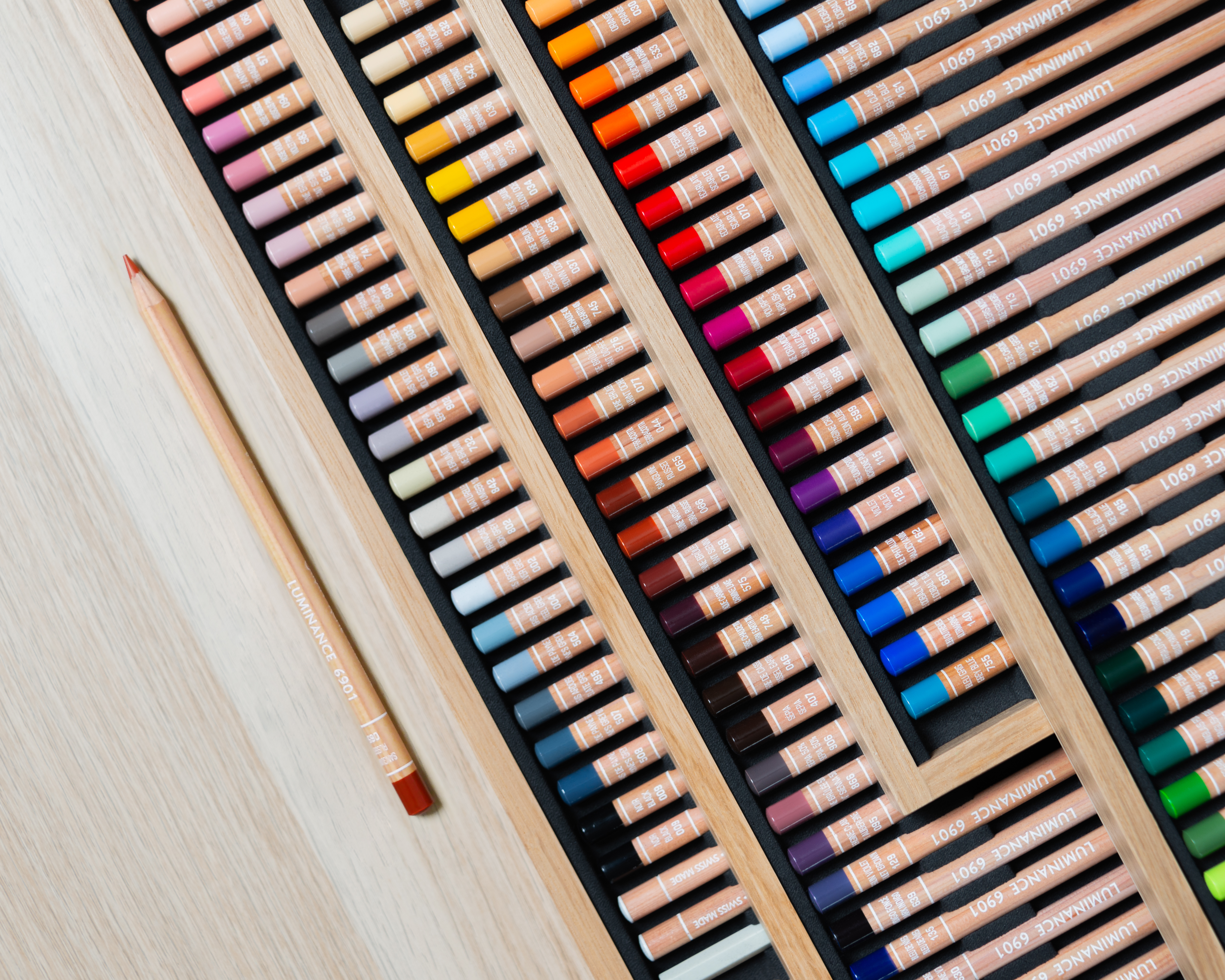 Close-up rows of Caran d’Ache Luminance 6901 pencils in wooden trays—100 lightfast colours for layering and blending.
