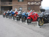 Condor Pit Stop/Trailer Wheel Chock, line of motorcycles parked on wheel chocks outside a rustic building, used for securing bikes during parking and trailer loading.