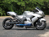 Brocks Performance Brocks Tiwinder Full Exhaust Street Baffle Blue Kawasaki ZX14R (06-20), silver sports motorcycle with blue exhaust pipe on an asphalt road with green trees in the background.