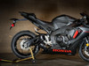 M4 Performance Exhausts M4 GP Black Slip-On Exhaust Honda CBR1000RR (17-26), mounted on a black sport motorcycle with a sleek design and red Honda logo, positioned indoors on a stand.