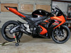 M4 Performance Exhausts M4 GP Black Slip On Exhaust Suzuki GSXR1000 (07-08), motorcycle with black and orange fairing, in a garage setting.