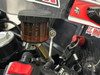 Schnitz Racing Motorcycle Performance Parts Ladybird Brake and Clutch Reservoir Bracket Kit, close-up view of the black and amber reservoir mounted on a motorcycle handlebar with associated components and red accents.