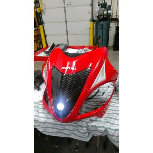 Montgomery Motorsports Carbon Fiber Headlight Insert Suzuki Hayabusa (08-21), red motorcycle fairing with carbon fiber headlight insert, displayed on a workbench in a garage.