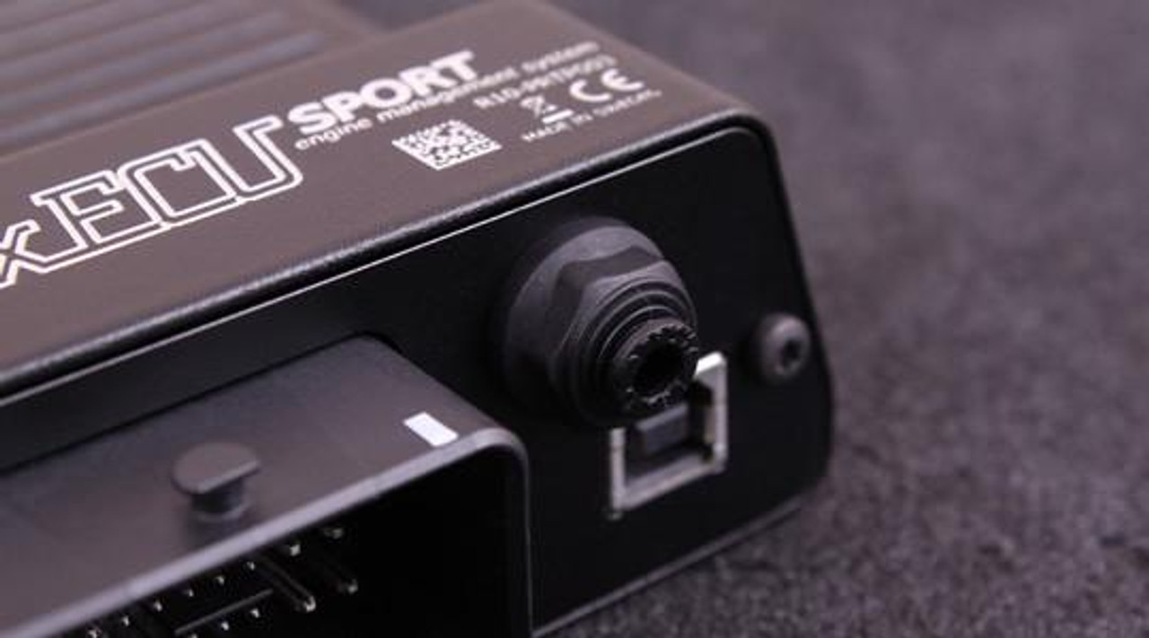 MaxxECU Sport Engine Control Unit, close-up view of the black automotive ECU with connectors on a dark surface. MaxxECU Sport Engine Control Unit, close-up view of the black automotive ECU with connectors on a dark surface.