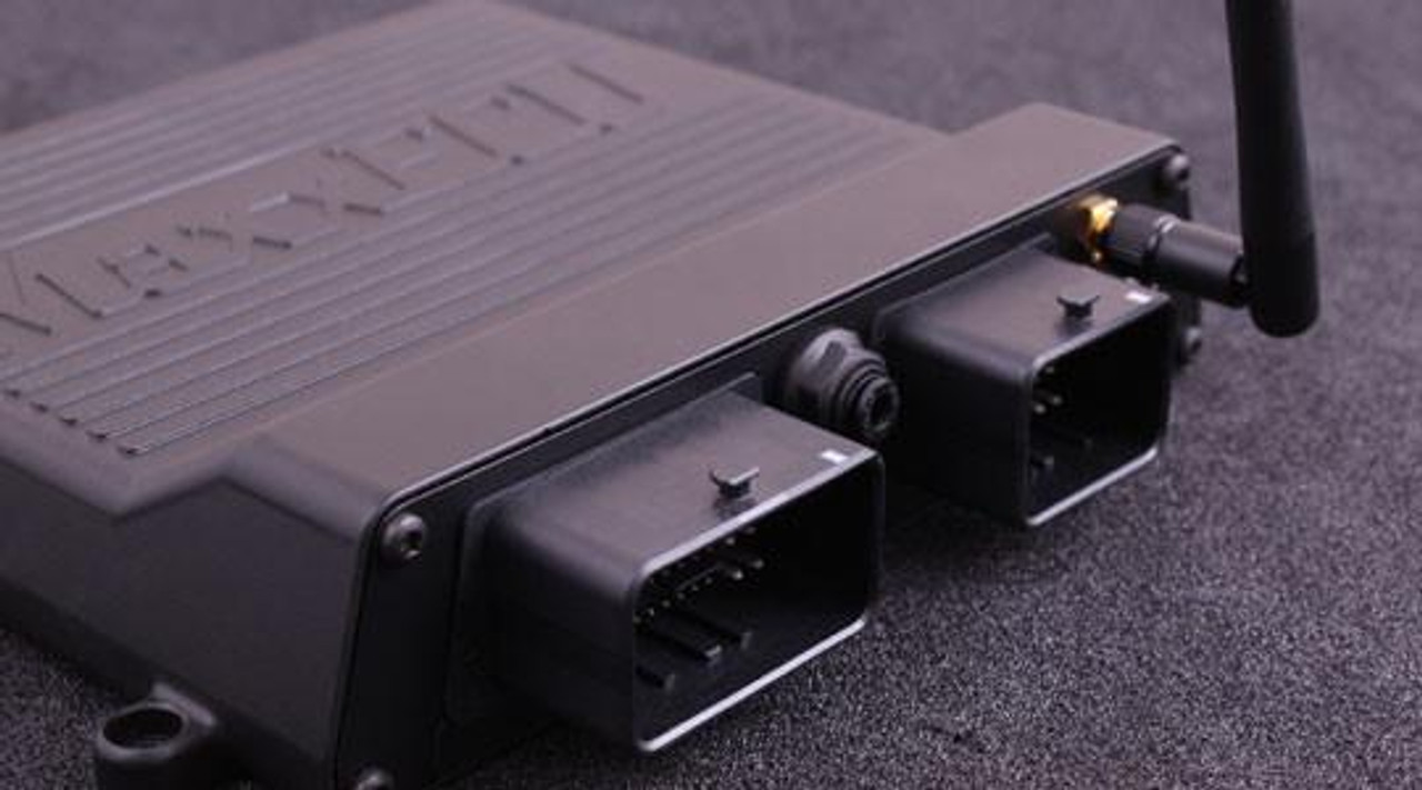 MaxxECU Race Engine Control Unit, close-up image of a black racing engine management module with connectors and antenna for high-performance vehicle engine control.