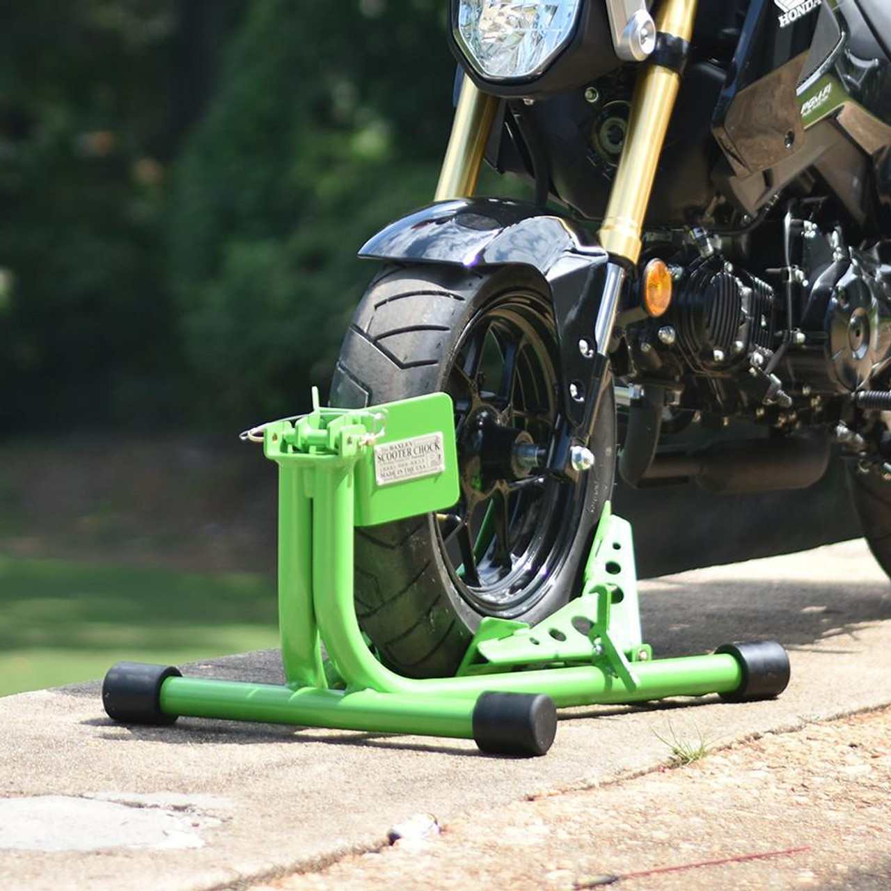 Baxley Scooter Chock, green motorcycle wheel chock securing a black motorcycle on a sidewalk.