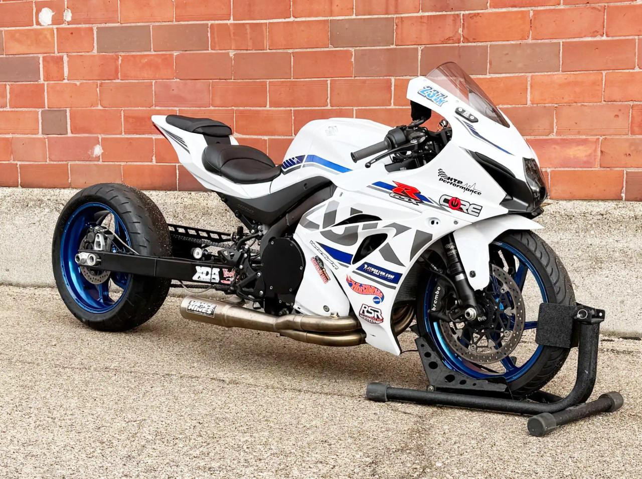 Vance & Hines Sidewinder Exhaust Suzuki GSXR-1000/R (17-25), motorcycle with custom white and blue racing livery parked outdoors against a brick wall.