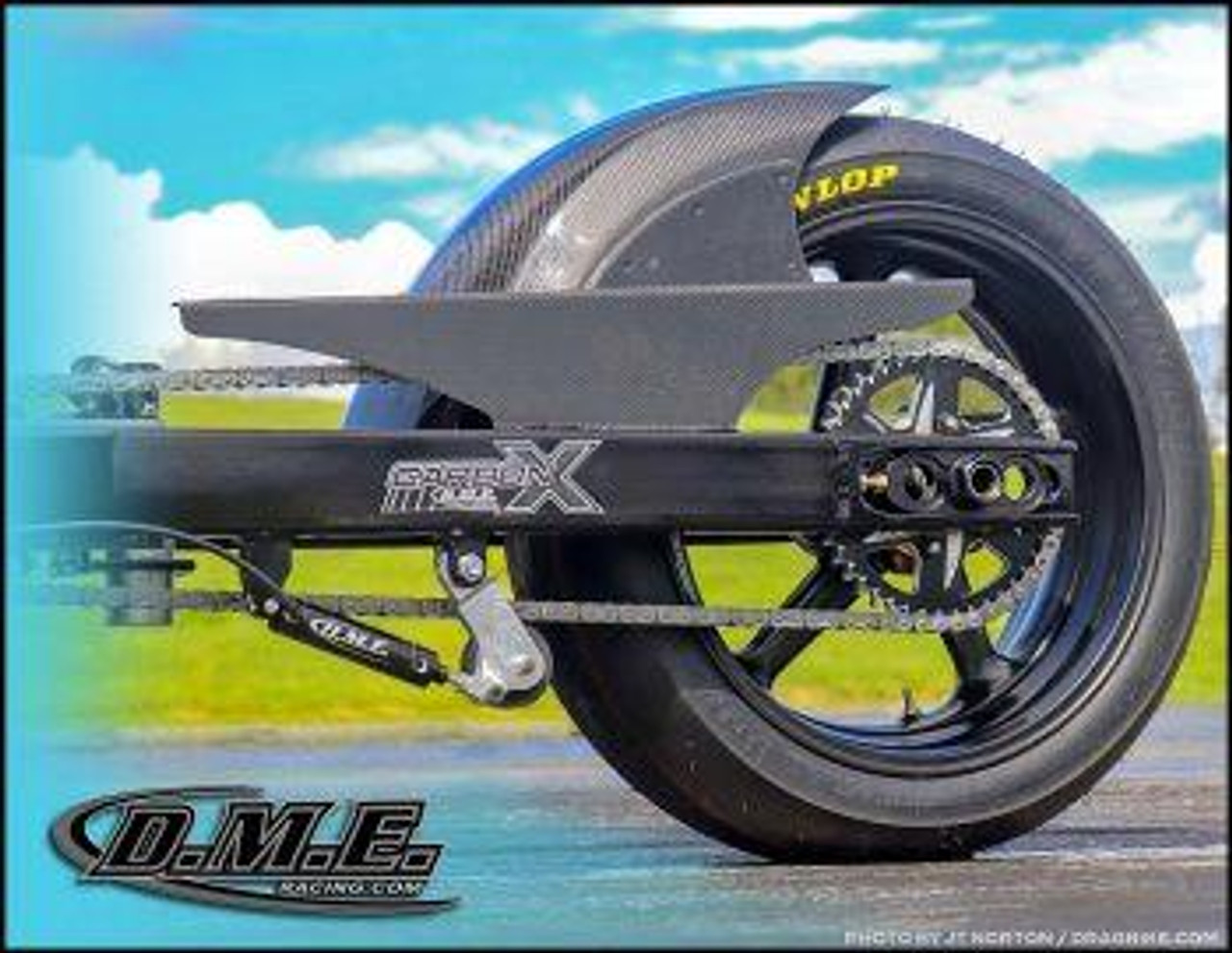 DME Air Ram Chain Tensioner Kit, close-up of motorcycle chain tensioner and rear wheel assembly against outdoor background.