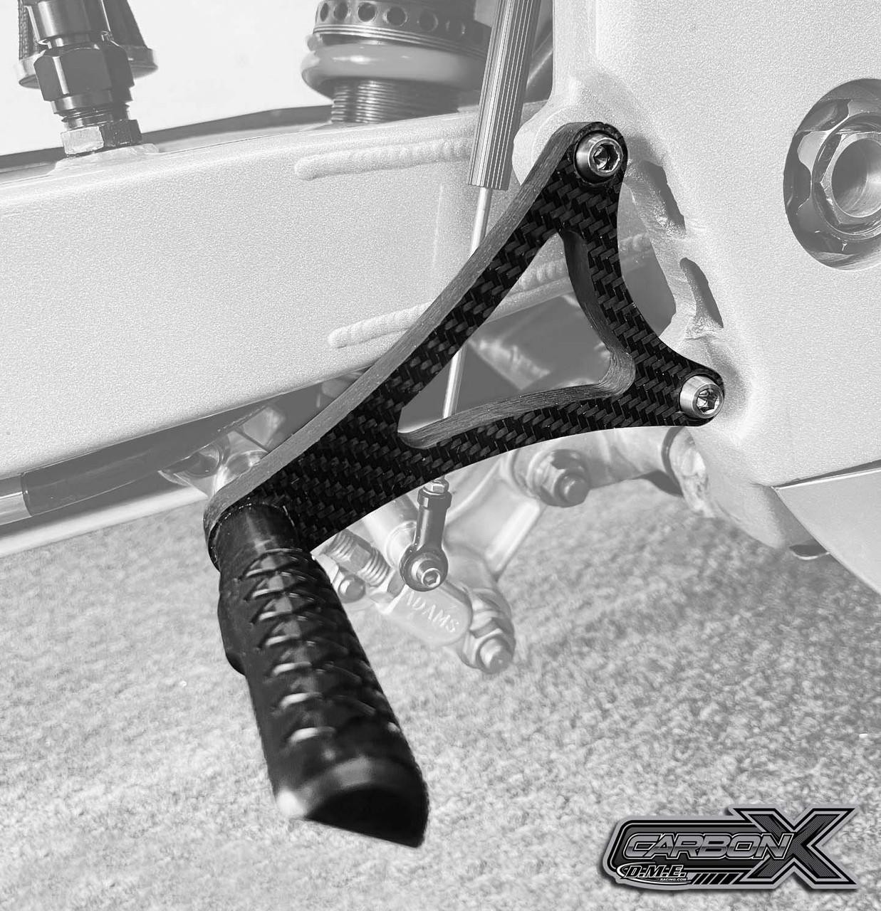 DME Rearsets, Grudge, Carbon Fiber, Kawasaki ZX-10R (06-10), close-up of black carbon fiber rearset with footpeg and mounting hardware attached to motorcycle frame.