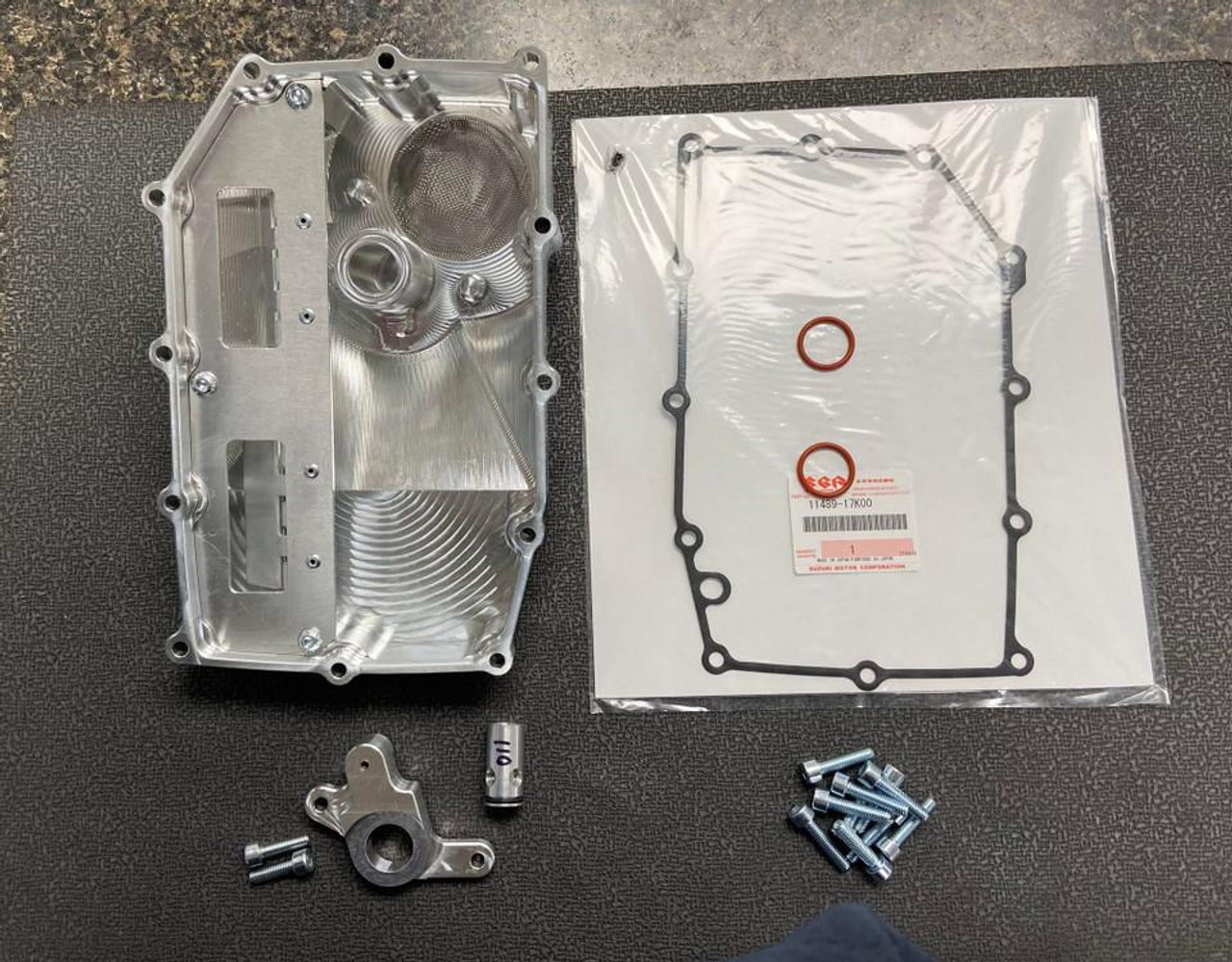 Brutal Performance Low Profile Billet Oil Pan Suzuki GSXR1000 (17-25) Direct Pickup, image showing a metallic aluminum oil pan with mounting bolts, gasket, and other components on a dark surface.