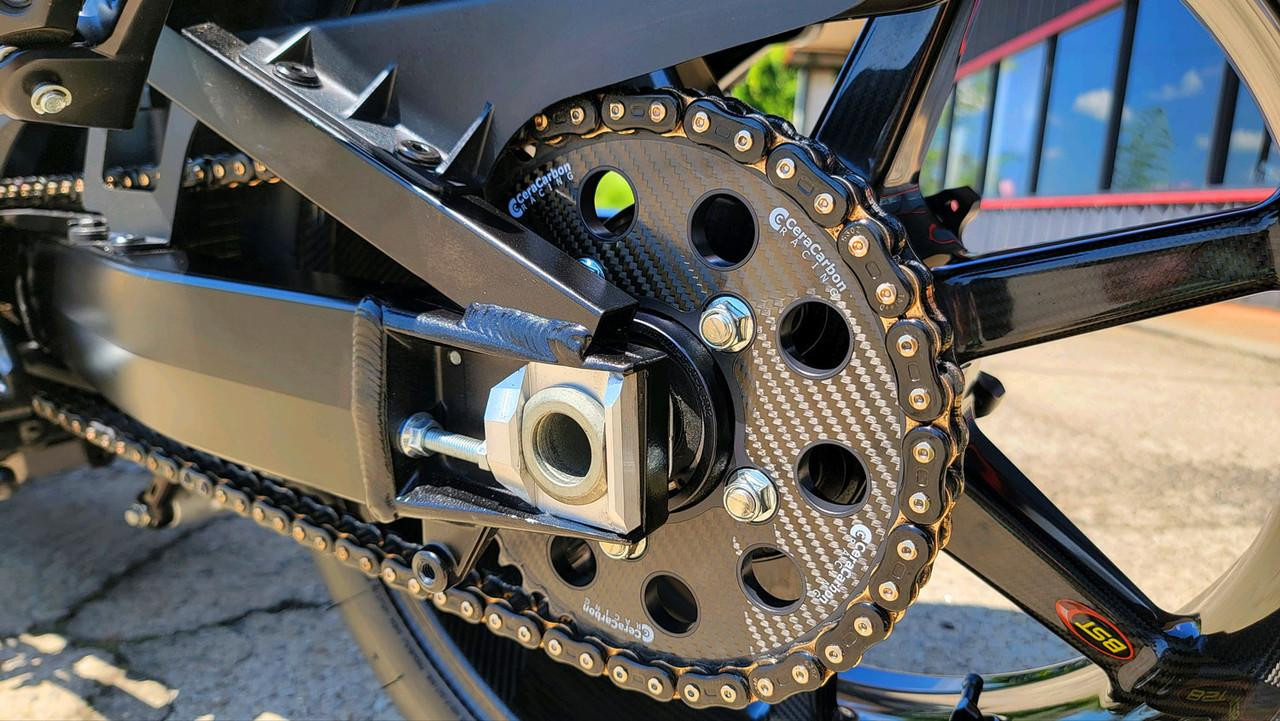 CeraCarbon Hybrid Rear Sprocket BST/Marvic/Coremoto 5 Bolt, 76mm OD, 100mm Bolt Circle, close-up of black carbon fiber sprocket with gold chain attached on a motorcycle.