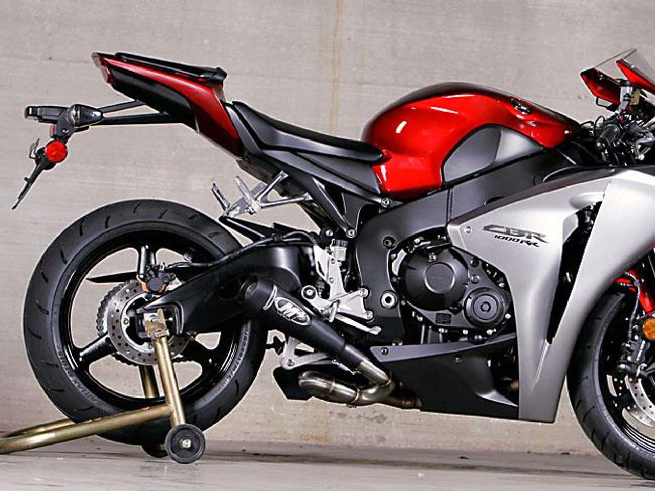 M4 Performance Exhausts M4 GP Black Slip On Exhaust Honda CBR1000RR (08-16), motorcycle with red and silver body and black exhaust system in a garage setting. M4 Performance Exhausts M4 GP Black Slip On Exhaust Honda CBR1000RR (08-16), motorcycle with red and silver body and black exhaust system in a garage setting.