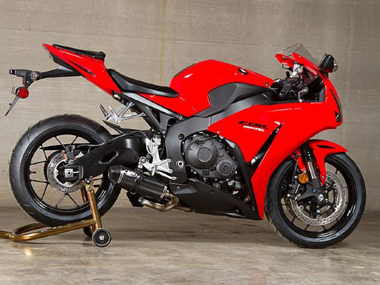 M4 Performance Exhausts M4 Street Slayer Carbon Slip On Exhaust Honda CBR1000RR (08-16), red sport motorcycle with black accents, positioned on a rear paddock stand against a concrete wall background.