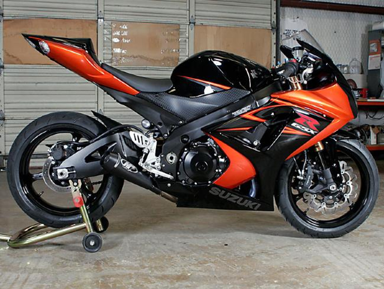 M4 Performance Exhausts M4 GP Black Slip On Exhaust Suzuki GSXR1000 (07-08), motorcycle with black and orange fairing, in a garage setting.