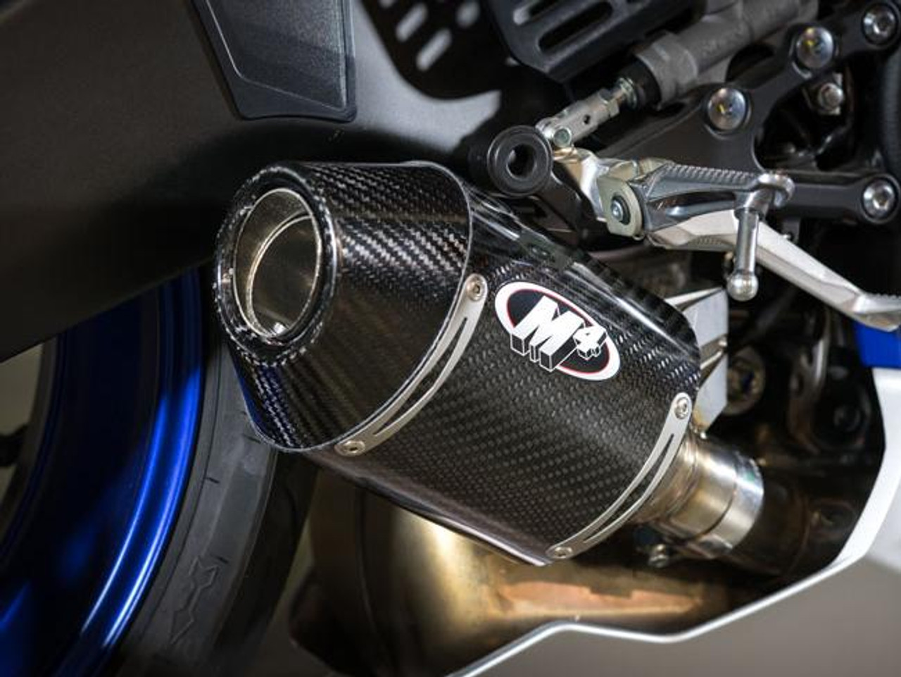 M4 Performance Exhausts M4 Carbon Fiber Street Slayer Slip On for Yamaha YZF-R6 2006-2020, close-up of the black carbon fiber muffler with logo, mounted on a motorcycle.