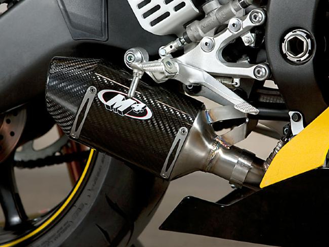 M4 Performance Exhausts M4 Carbon Fiber Street Slayer Slip On Yamaha YZF-R6 w/ Muffler Box Eliminator, close-up of the carbon fiber exhaust with logo and metallic components on a yellow and black Yamaha motorcycle. M4 Performance Exhausts M4 Carbon Fiber Street Slayer Slip On Yamaha YZF-R6 w/ Muffler Box Eliminator, close-up of the carbon fiber exhaust with logo and metallic components on a yellow and black Yamaha motorcycle.