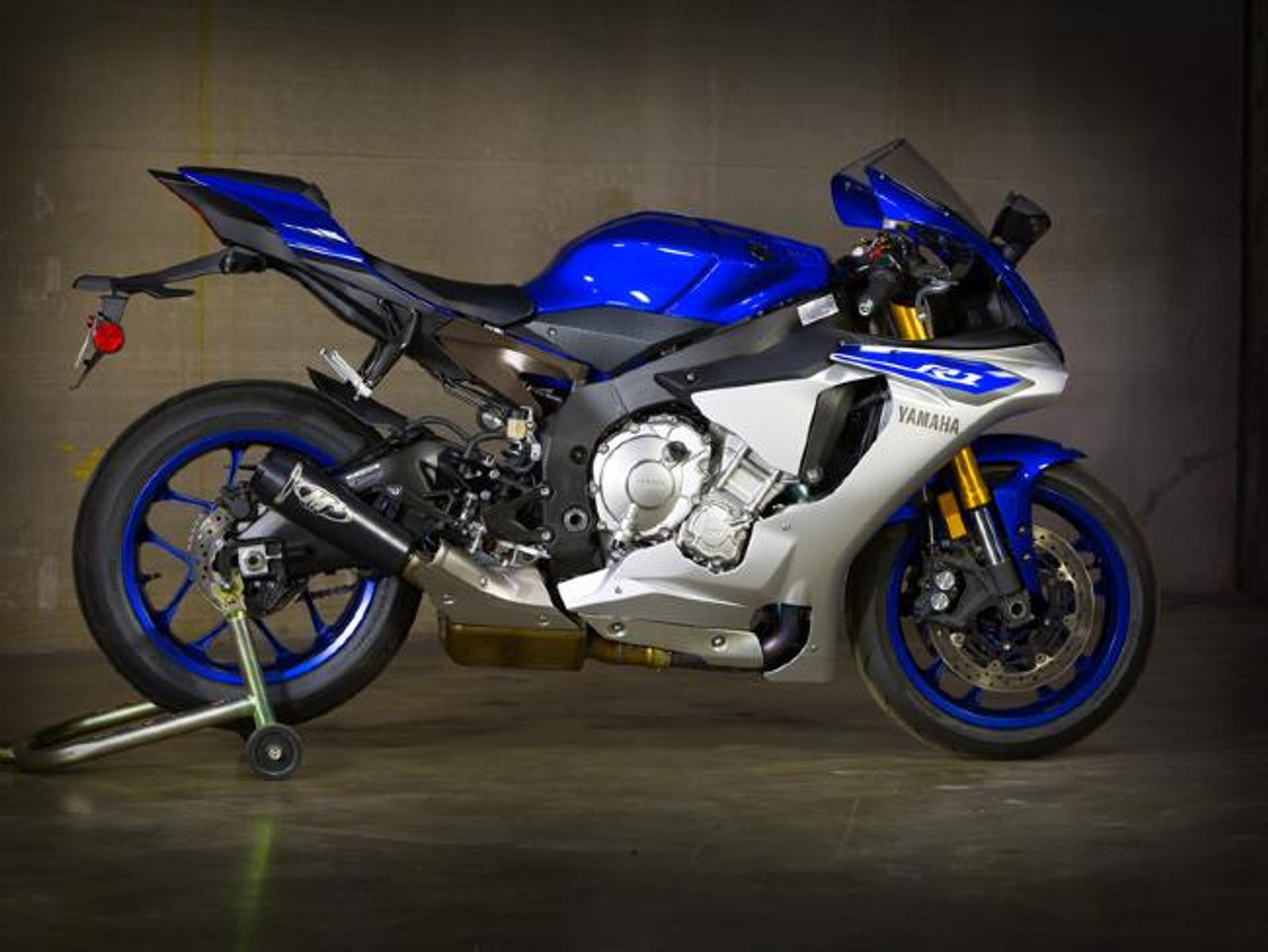 M4 Performance Exhausts M4 GP2 Black Slip On Exhaust Yamaha YZF-R1 (15-24): Blue and black Yamaha YZF-R1 motorcycle parked indoors with a stand supporting the rear wheel, showcasing the modern design and performance exhaust system.