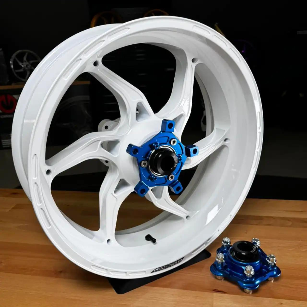 Coremoto Apex-6 Forged Aluminum Wheels Yamaha YZF-R1 (15-26), a white motorcycle wheel with a blue hub and a separate blue hub component placed on a wooden surface.