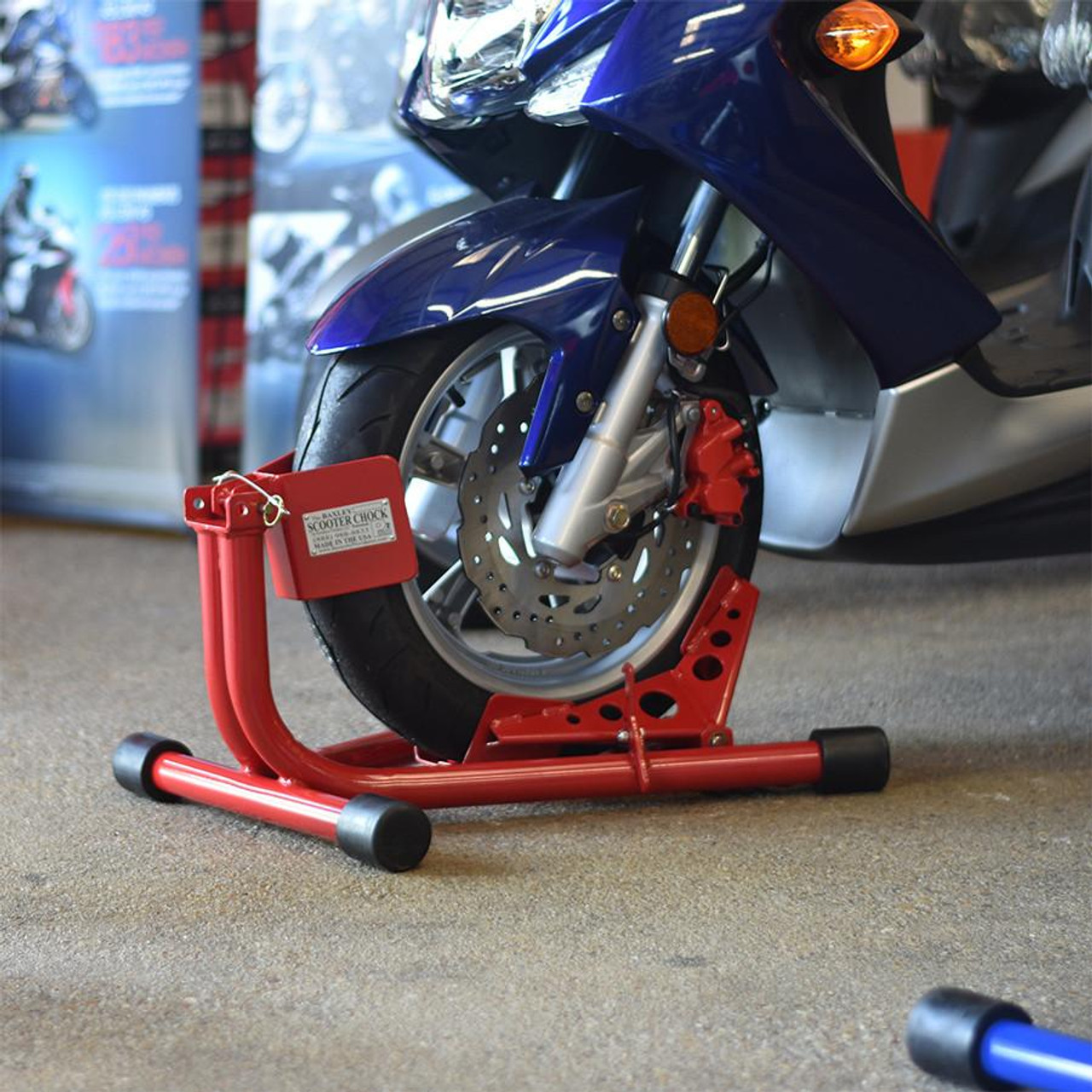 Baxley Small Bore Scooter Chock, red motorcycle wheel chock securing a blue scooter's front wheel for stabilization.