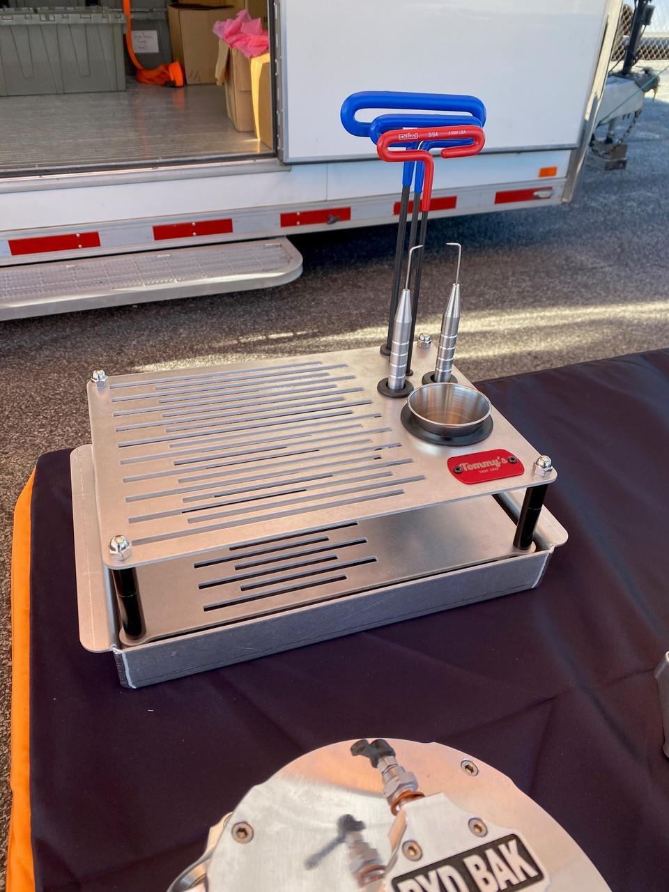 Tommy's Chop Shop Clutch Maintenance Tray, a stainless steel tray with slotted surface and standing tools with colored handles on a black surface, outdoors.
