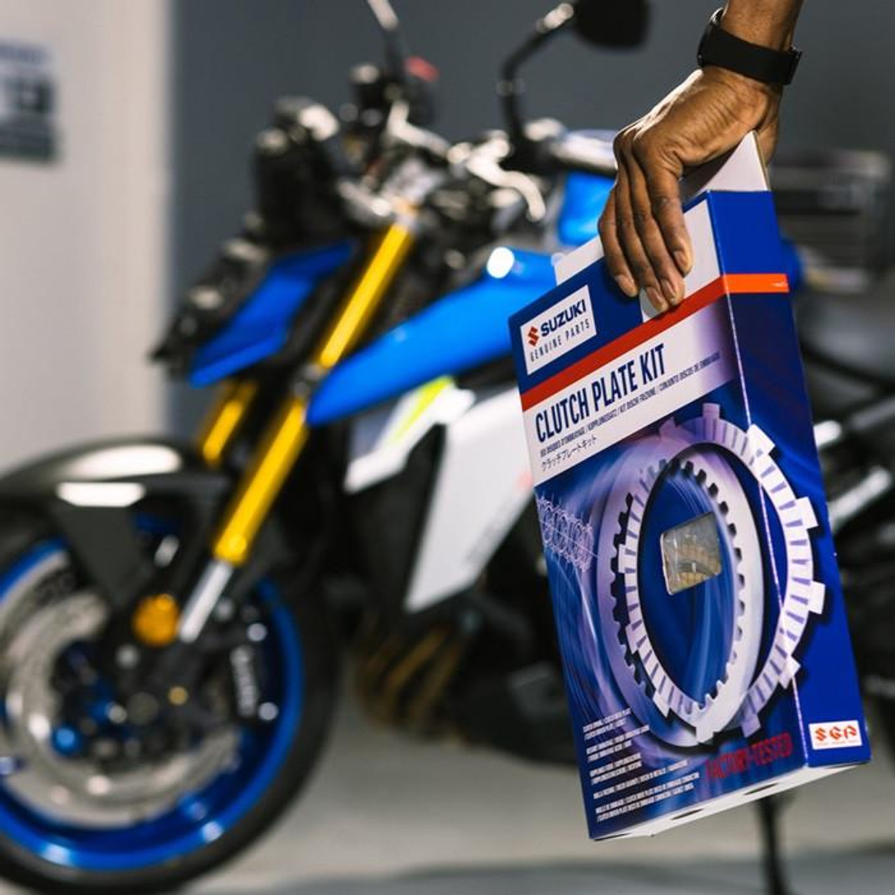 Suzuki OEM Complete Clutch Kit Suzuki GSXR600 (06-07), product box being held by a person with a motorcycle in the background.